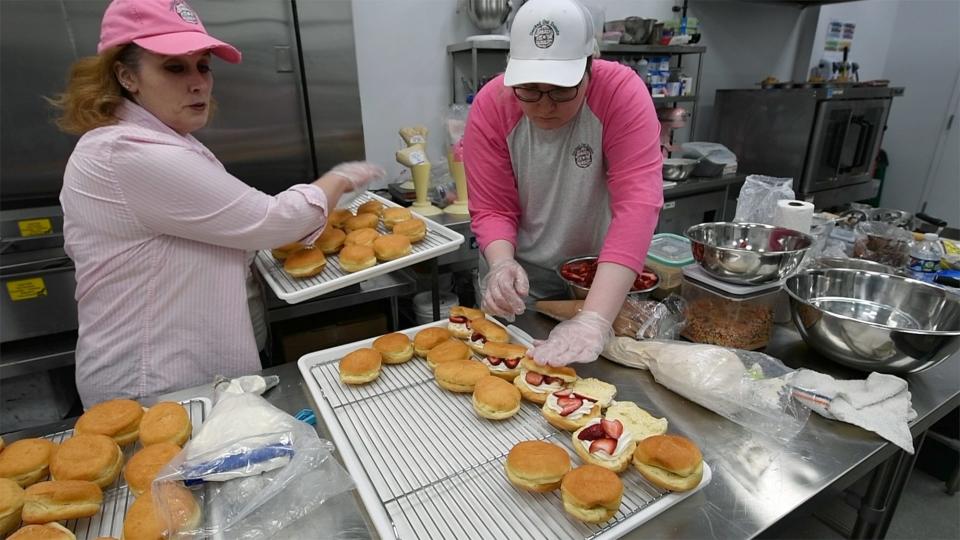 Amy Lovisone, left, and her daughter, Ella rush out a second run of strawberry shortcake doughnuts after a line of people at the door before opening wiped them out.