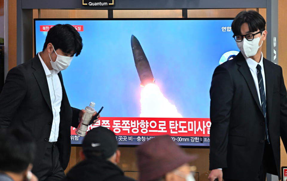 People walk past a television screen showing a news broadcast with file footage of a North Korean missile test, at a railway station in Seoul on October 4, 2022.