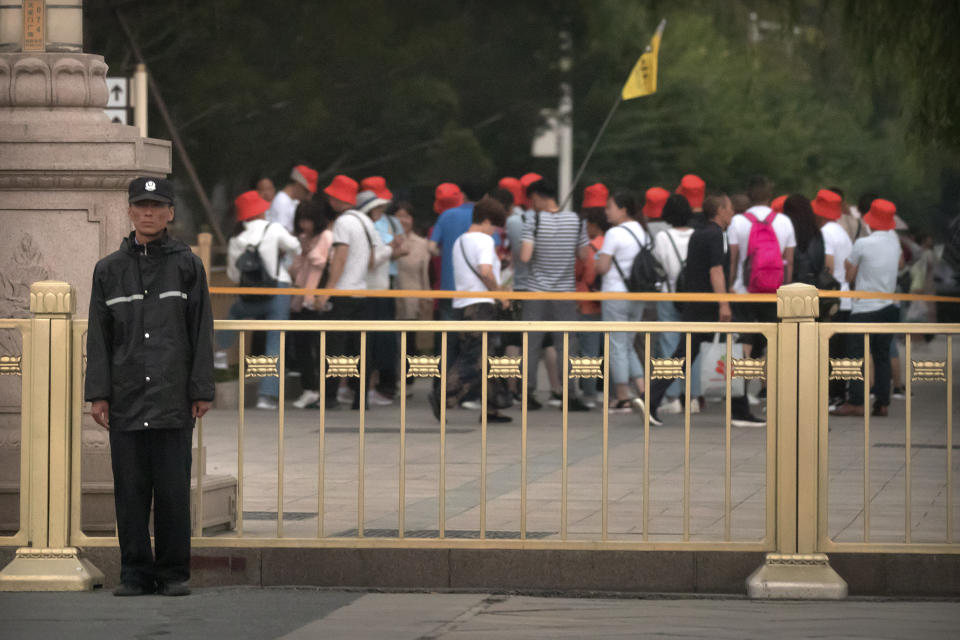 A security official stands guard as a tour group walks along a street next to Tiananmen Square in Beijing, Tuesday, June 4, 2019. Chinese authorities stepped up security Tuesday around Tiananmen Square in central Beijing, a reminder of the government's attempts to quash any memories of a bloody crackdown on pro-democracy protests 30 years ago. (AP Photo/Mark Schiefelbein)