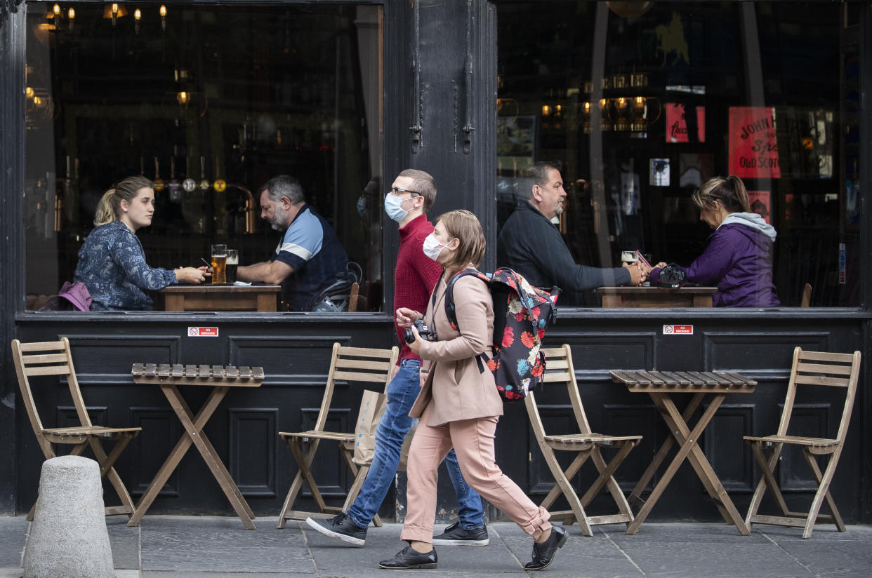 People wearing protective face masks walk past a bar in Edinburgh city centre, after First Minister Nicola Sturgeon announced a range of new measures to combat the rise in coronavirus cases in Scotland. (Photo by Jane Barlow/PA Images via Getty Images)