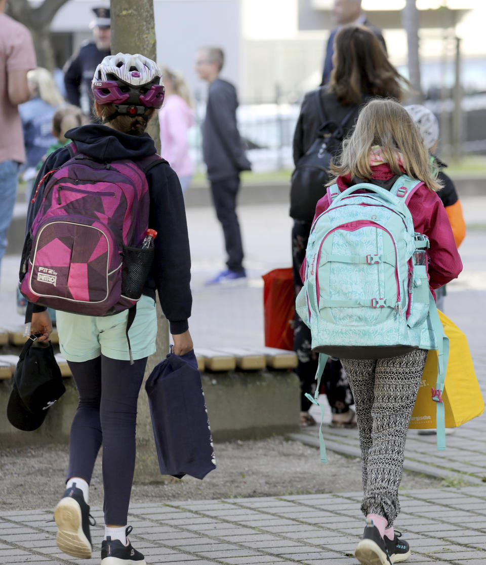 Children make their way to school by their parents in Rostock, Germany Monday, Aug. 3, 2020 as Mecklenburg-Western Pomerania is the first federal state to resume regular school operations throughout the state. About 150,000 students are expected to attend their schools. (Bernd Wuestneck/dpa via AP)