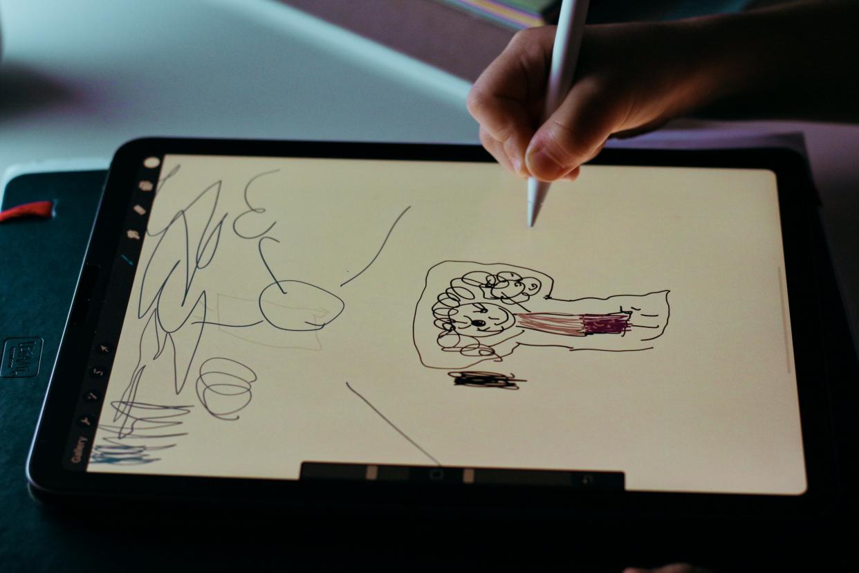  A close up of a child's hand as they use a stylus to draw on a tablet. 