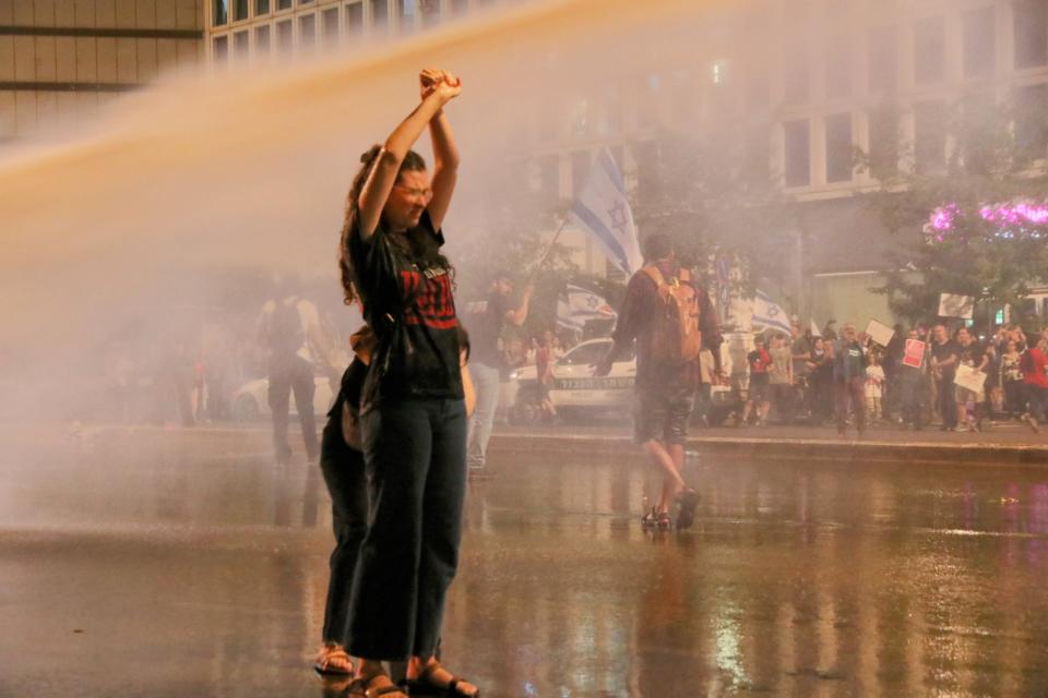 A protestor calling for hostages to be returned in a deal near Begin Gate in Tel Aviv under the spray from a police water canon (Amir Yaacobi)