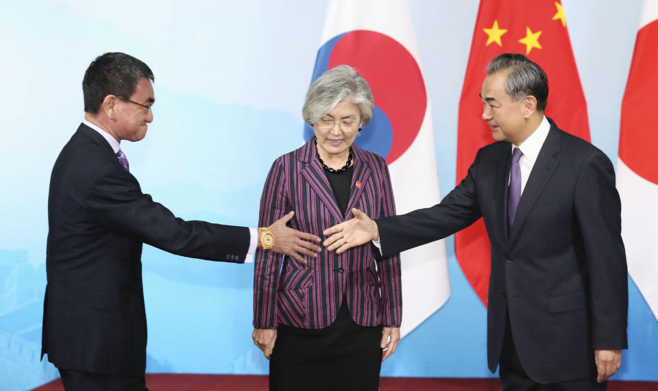 Chinese Foreign Minister Wang Yi, right, shakes hands with Japanese Foreign Minister Taro Kono, left, as South Korean counterpart Kang Kyung-wha, center, looks on, ahead of their meeting in Beijing Wednesday, Aug. 21, 2019. (Kyodo News via AP)