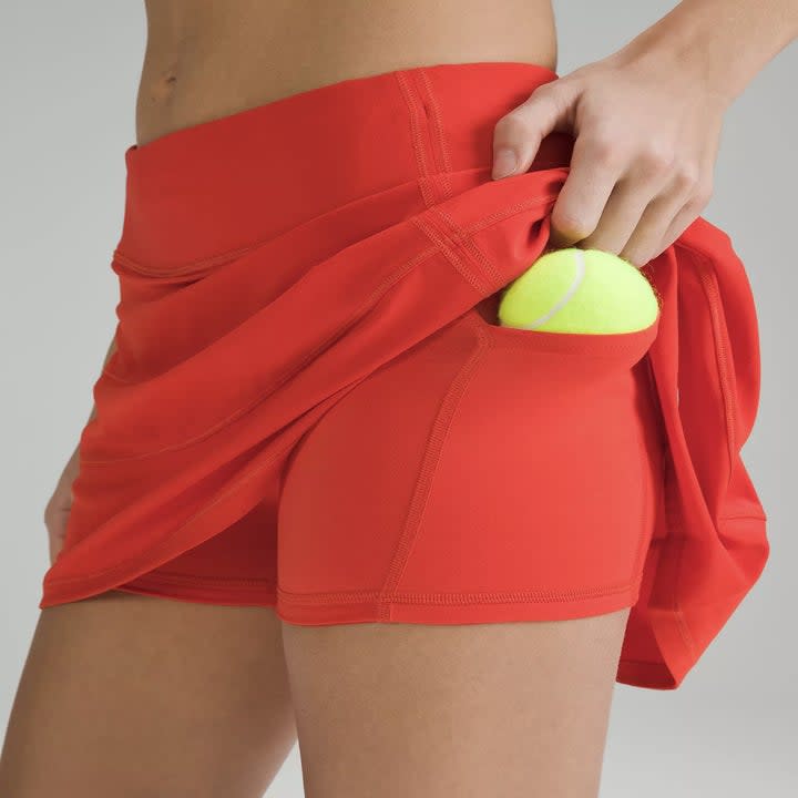 someone putting tennis ball in side pocket of red skort