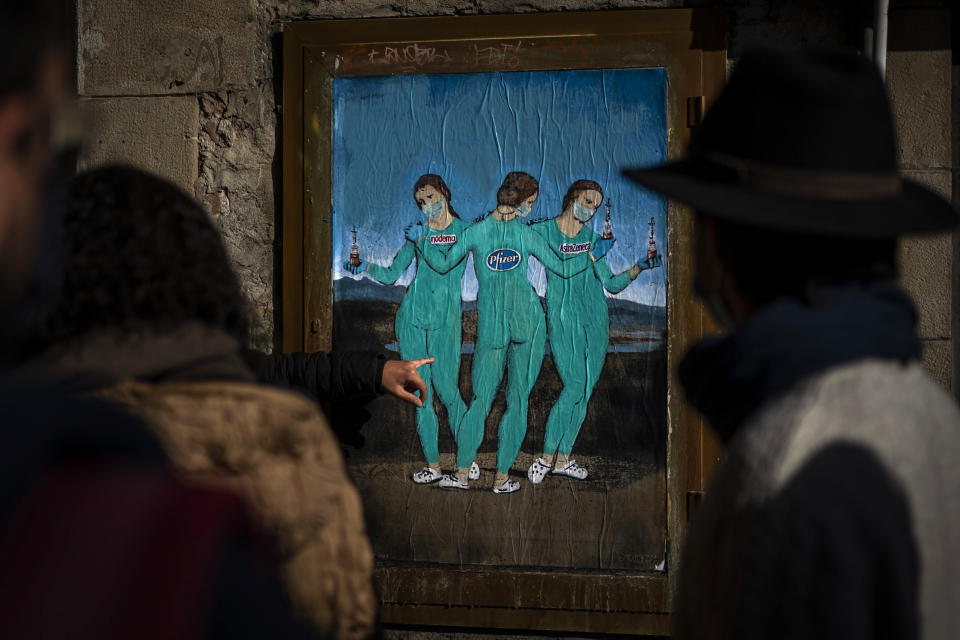 People look at a painting by Italian street artist TvBoy named "The three Vaccines" depicting The Three Graces by Italian painter Raphael in Barcelona, Spain, Friday, Jan. 22, 2021. Although health authorities believe that the surge of coronavirus infections is waning, the rate of contagion has shot to over three times the extreme risk level, dangerously straining the health system. (AP Photo/Emilio Morenatti)