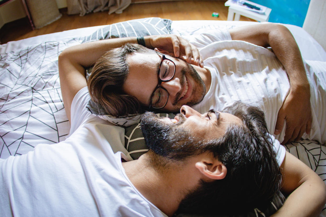 Gay couple lying in bed together smiling and embracing. (Getty Images)