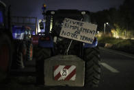 A sign on a tractor reads "live simply from our work" at a highway barricade in Aix-en-Provence, southern France, Tuesday, Jan. 30, 2024. France's protesting farmers encircled Paris with traffic-snarling barricades Monday, using hundreds of lumbering tractors and mounds of hay bales to block highways leading to France's capital to pressure the government over the future of their industry. (AP Photo/Daniel Cole)