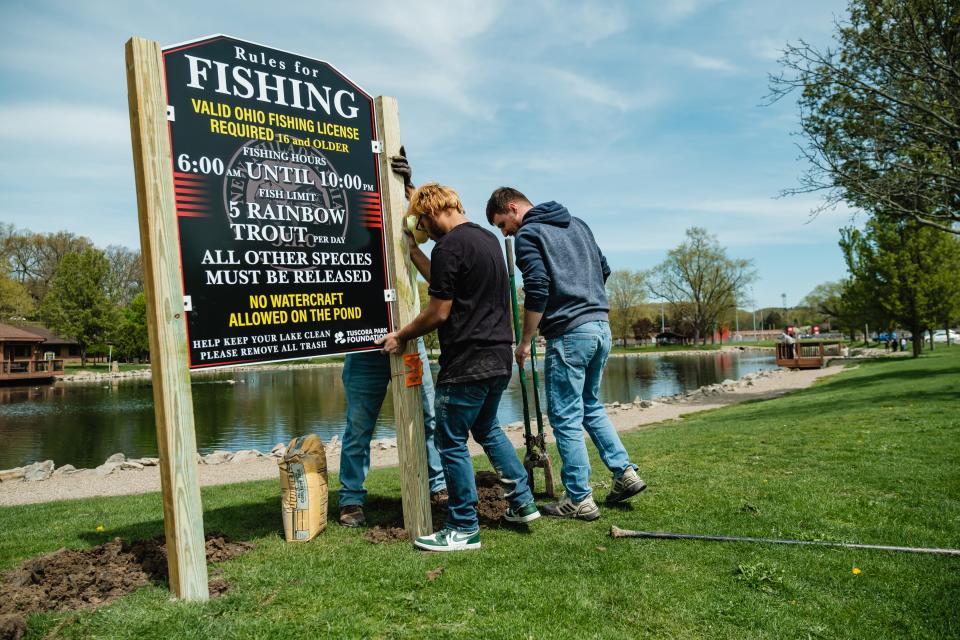 Lightning Signs workers install new signage Thursday, April 27, 2023, at Tuscora Park in New Philadelphia in anticipation of the first trout derby there. Pictured are, from left, Mikey Meese and Leroy Hartline. Behind the sign is Bill Martin.