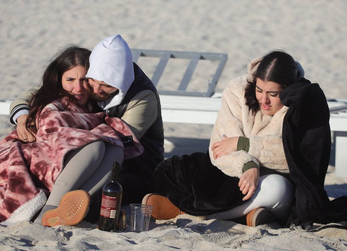 Beachgoers Jennifer Quintana, 23, and Cesar Reyes, 22, center, and Gabriela Alcantara, 20, left, keep warm while enjoying the sunrise in South Beach during a January 2022 cold wave that sent temperatures into the 40s in South Florida.