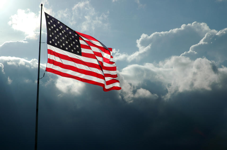 Back-lit American flag waving in the wind with a storm front moving in