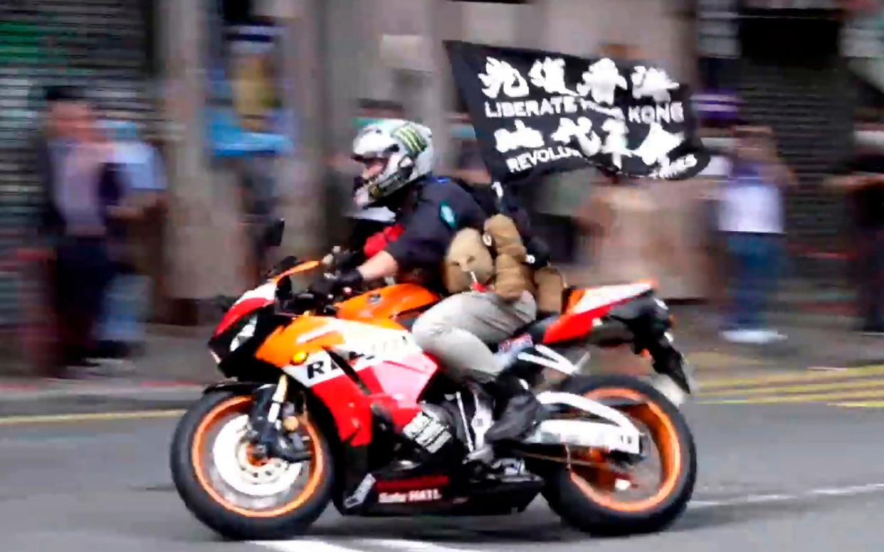 Tong Ying-kit on a motorcycle while carrying a flag reading "Liberate Hong Kong, Revolution of our times" during a protest in Hong Kong on July 1, 2020 - Cable TV Hong Kong 