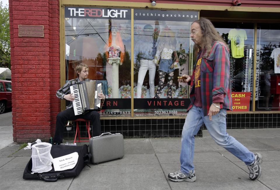 This April 30, 2013, image shows a street musician and passerby outside a vintage clothing store on Hawthorne Boulevard in Portland, Ore. Hawthorne is known for its funky vintage clothing stores, and is a great place for tourists to visit to soak up the people-watching scene, whether or not they’re in the market for recycled fashions. (AP Photo/Don Ryan)