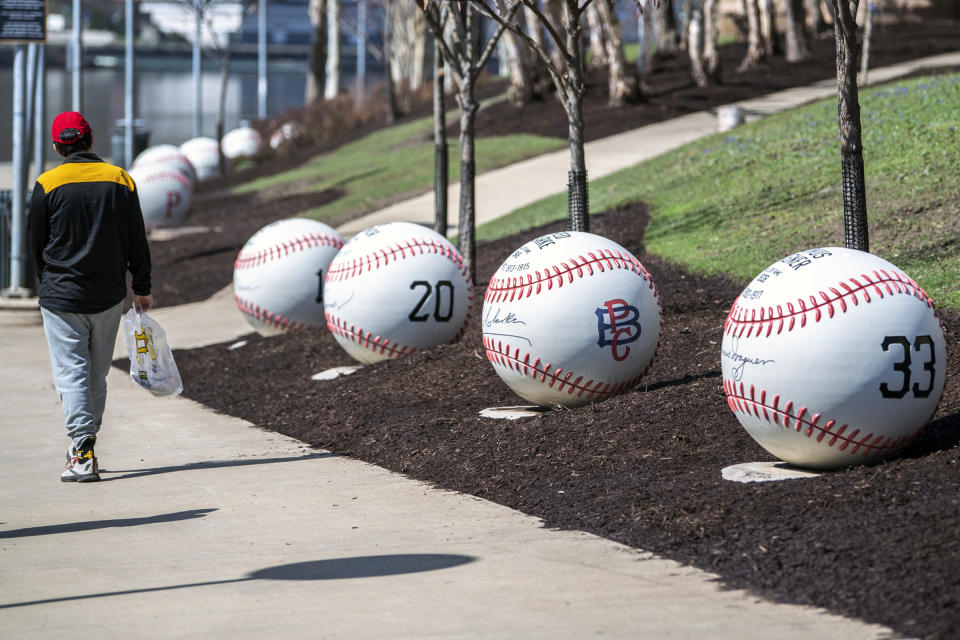 A baseball fan walks by baseball statues commemorating Hall of Fame players ahead of the Pittsburgh Pirates home opener against the Chicago Cubs, Tuesday, April 12, 2022, on the Three Rivers Heritage Trail on the North Shore in Pittsburgh. (Alexandra Wimley/Pittsburgh Post-Gazette via AP)