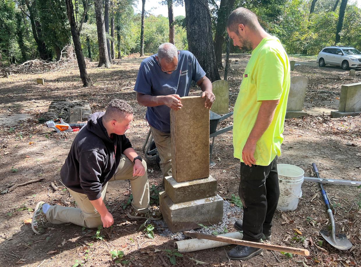 Noah Meredith, kneeling, watches as Clarence Wellman of Lincoln Hill Cemetery shows how a headstone fits on a base at Southern Hill Cemetery as Mark Galbreath of Lincoln Hills looks on.