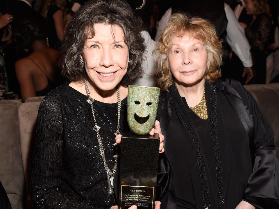 Lily Tomlin and Jane Wagner sitting in a theatre holding up an award