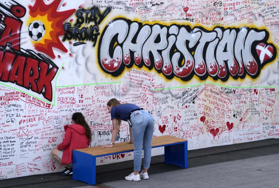 People leave well wishes at a graffiti for Danish player Christian Eriksen on a wall at the fanzone in Copenhagen, Denmark, Monday, June 14, 2021. Eriksen remains in hospital after he collapsed on the pitch during the European Championship game against Finland on Saturday and needed CPR from medical staff before regaining consciousness. (AP Photo/Martin Meissner)