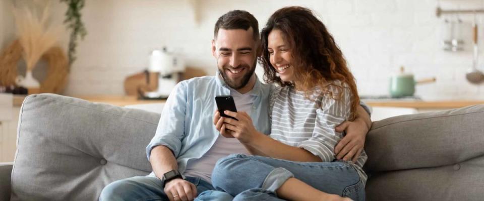 Happy young wife showing cellphone to laughing husband.