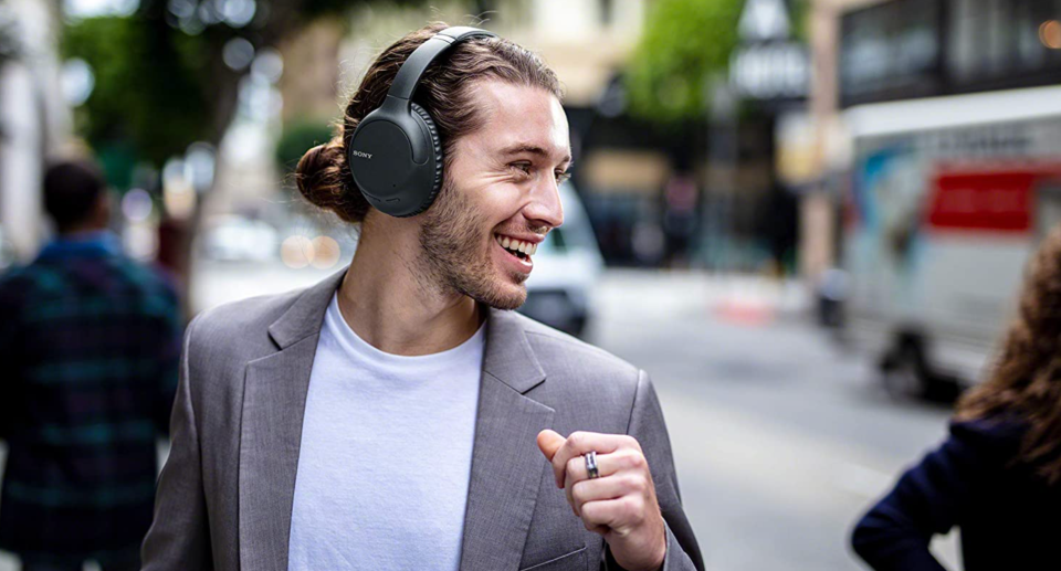 man wearing blazer and t-shirt and black over-ear sony headphones smiling on street, early amazon canada boxing day deal on sony headphones