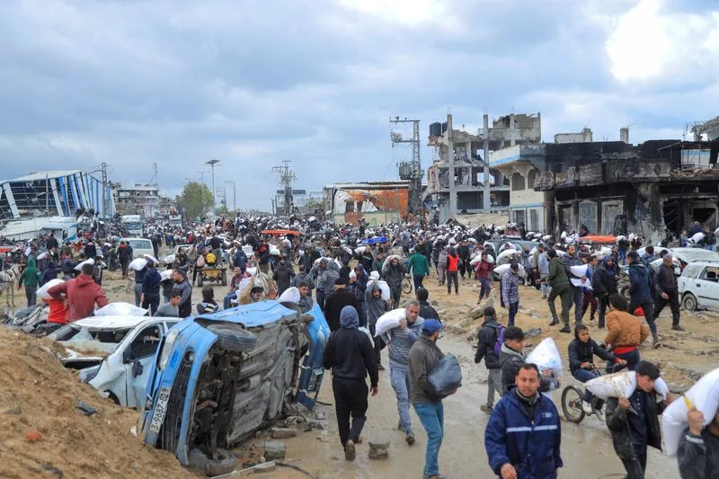 Palestinians carry bags of flour they grabbed from an aid truck near an Israeli checkpoint, in Gaza City