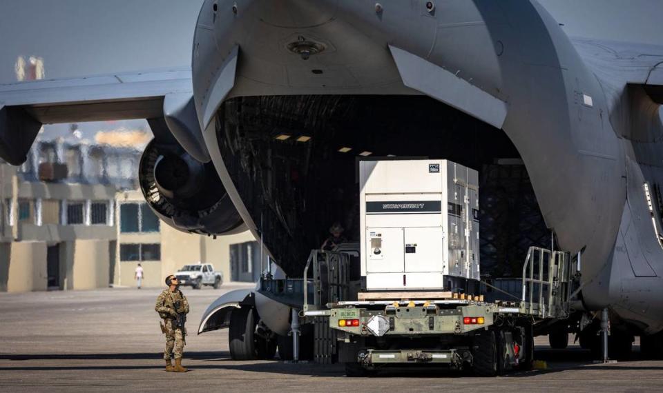 A United States serviceman, left, stands guard on Wednesday, May 15, 2024, as supplies are offloaded from a U.S. Air Force C-17 cargo plane on the tarmac at Toussaint Louverture International Airport in Port-au-Prince, Haiti. The plane was carrying supplies for the camp being built for Kenyan police officers who will lead a Multinational Security Support mission into Haiti.
