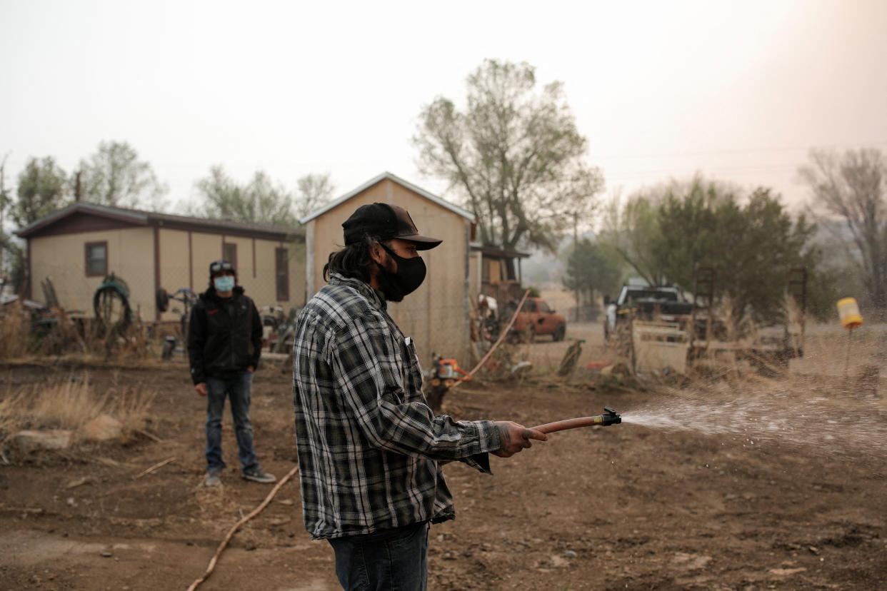 A man wearing a face mask is seen spraying water on his property.