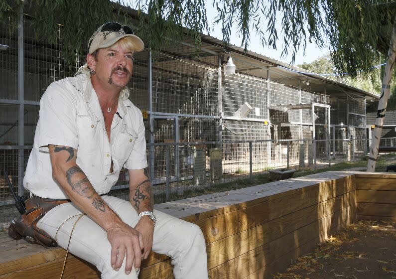 A man with blond hair in an all-white outfit sitting on a ledge by tiger cages