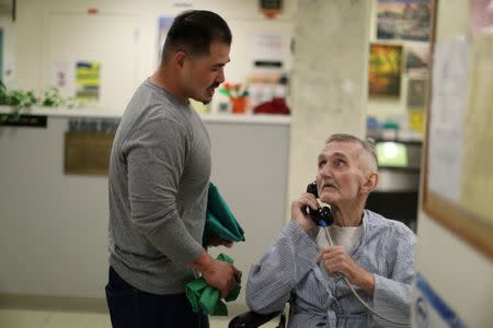 Pastoral Care Services Worker and inmate Kao Saephanh (L) helps inmate Joseph Morrow, 69, who has bladder cancer, make a phone call in the hospice at the California Medical Facility prison in Vacaville, California, U.S., May 22, 2018. REUTERS/Lucy Nicholson