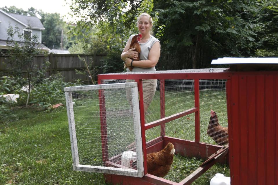In this Sunday, Aug. 11, 2013 photo, Sandy Schmidt, who owns a portable chicken coop, poses with her chickens at her home in Silver Spring, Md. Schmidt compares the time required for basic chicken care to a more familiar pet. "It's about like having a cat," she says. "Make sure they have food and water every day, scoop out the coop - like a litter box - and let them out of the coop." (AP Photo/Charles Dharapak)