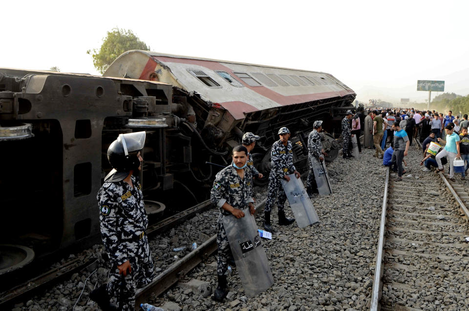 Security forces stand guard as people gather at the site where a passenger train derailed injuring at least 100 people, near Banha, Qalyubia province, Egypt, Sunday, April 18, 2021. At least eight train wagons ran off the railway, the provincial governor's office said in a statement. (AP Photo/Tarek Wagih)