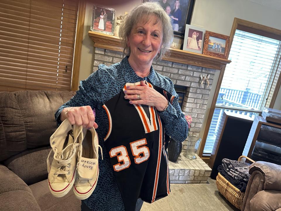 Nancy Schmitz poses with the jersey and sneakers she wore when she played six-on-six basketball at Elk Horn-Kimballton High School in the 1960s at her home in La Vista, Neb., Monday, March 4, 2024. Schmitz, then Nancy Wolken, was a third-team all-state pick in 1968. (AP Photo/Eric Olson)