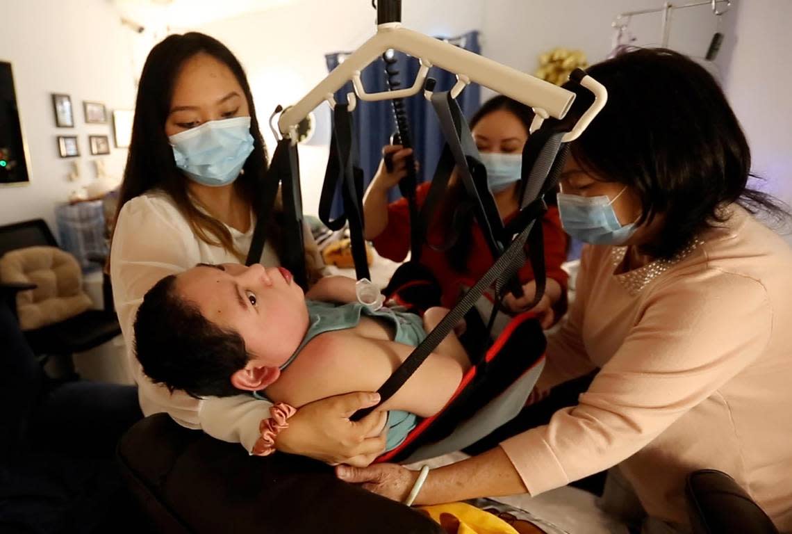 Justin Nguyen, 24, is supported by his sisters, Jennifer and Jessica Pham, and his mother, Julie Nguyen, as they use a Hoyer lift to help transfer him from his bed to a chair in his bedroom in their Jacksonville home. Justin suffered severe brain damage at birth.