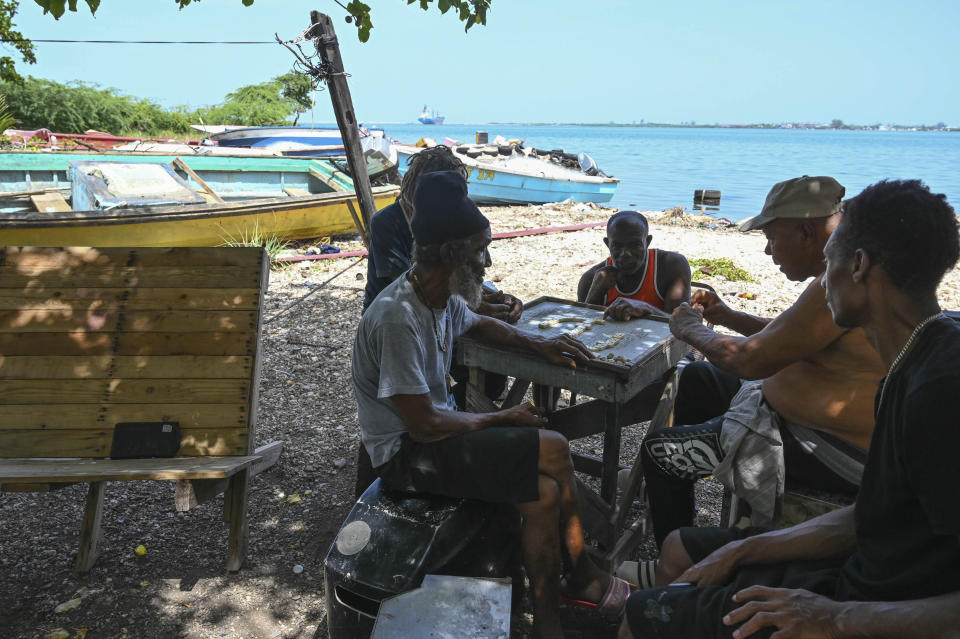 Pescadores juegan al dominó después de sacar sus barcos del agua para protegerlos del huracán Beryl en Kingston, Jamaica, martes 2 de julio de 2024. (AP Foto/Collin Reid)