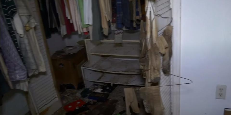 A photo of a dark and dirty closet, with hangers, clothes, and furniture askew.