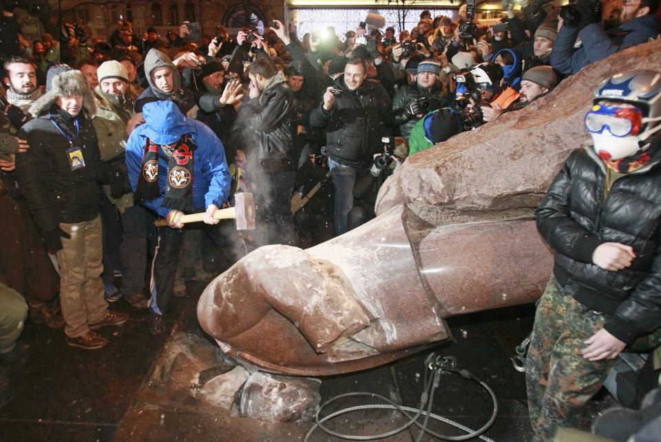 A man holds a sledgehammer as he smashes a statue of Soviet state founder Vladimir Lenin, which was toppled by protesters during a rally organized by supporters of EU integration in Kiev