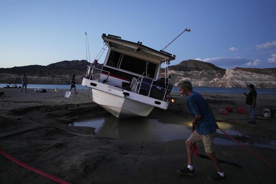 Craig Miller arrastra una manguera para tratar de desatascar su casa flotante, que quedó varada en el lago Mead al bajar el nivel de las aguas en medio de una sequía. Foto del 23 de junio del 2022. (AP Photo/John Locher)