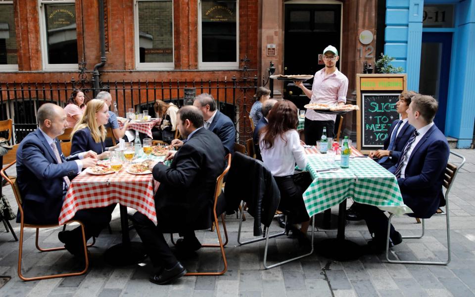 A waiter serves pizzas as diners sit at tables outside a restaurant in London on August 3 - TOLGA AKMEN/AFP