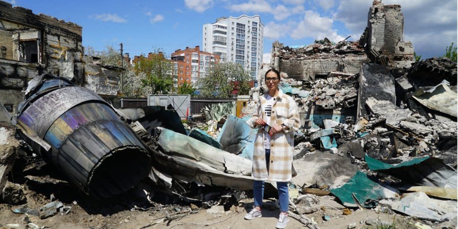 Yulia Grebneva stands near the ruins of her house and the wreckage of an enemy plane, which still remains in the yard