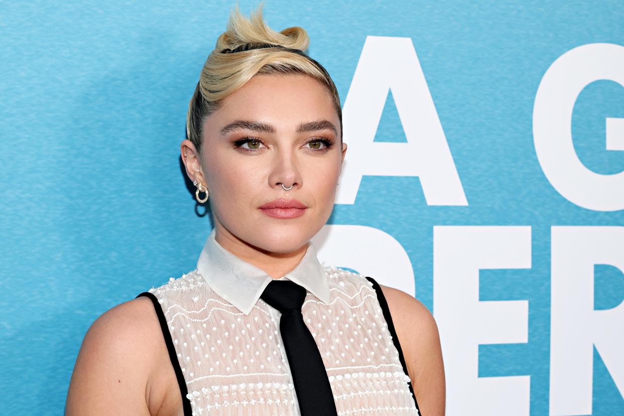 Florence Pugh wears a white shirt and black tie in front of a blue backdrop at "A Good Person" New York screening.