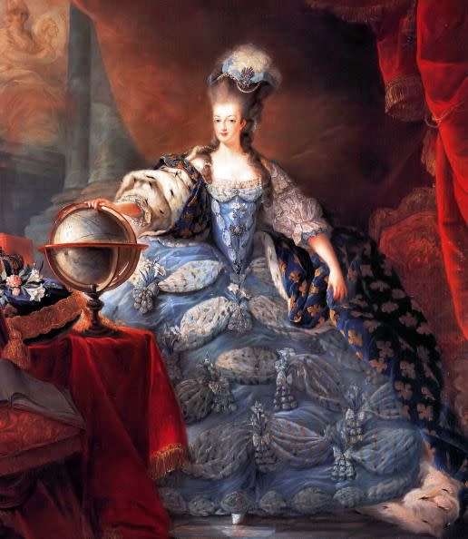 marie antoinette wearing a large blue dress and placing her hand on a globe