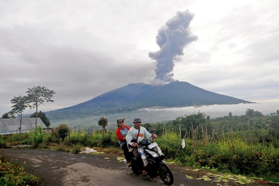 Motorists ride past by as Mount Marapi spews volcanic materials during its eruption in Agam, West Sumatra (AP)