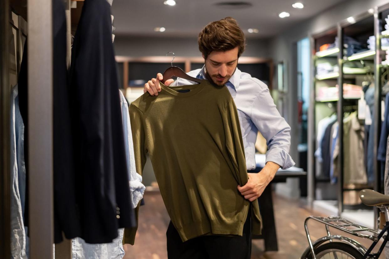 Latin american guy trying out a sweater on top at a men's clothing store - Consumerism concepts