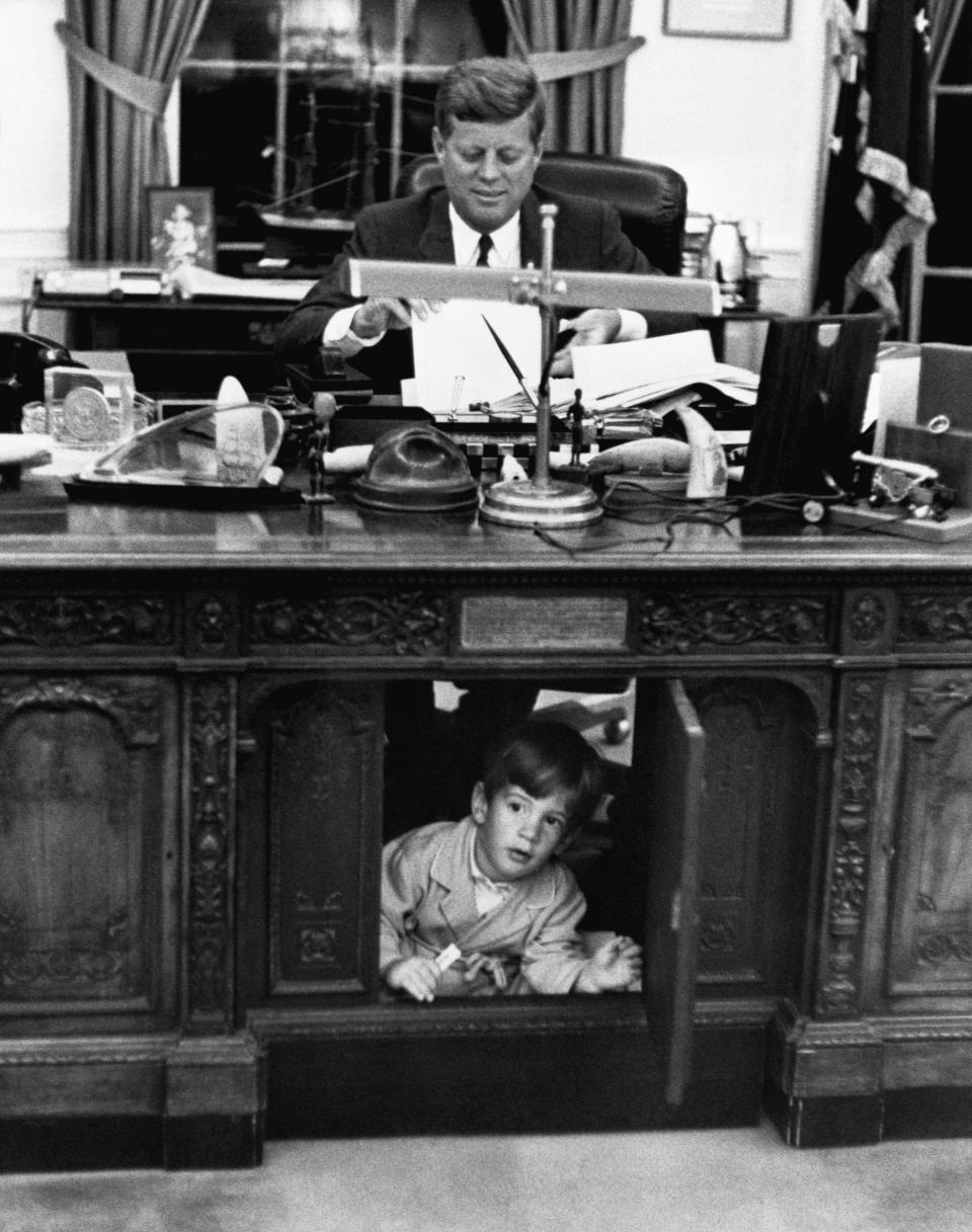 John Kennedy Jr. peers through an opening of the desk in the Oval Office in 1962.