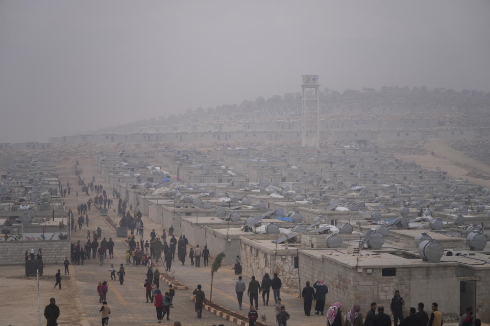 Syrians walk along in a refugee camp for displaced people run by the Turkish Red Crescent in Sarmada district, north of Idlib city, Syria, Friday, Nov. 26, 2021. Row upon row of tents, brick homes and other structures with water tanks on top dot the town of Sarmada near the border with Turkey, making up a series of huge informal refugee camps. Women cook, children play, men go to work, pray and discuss politics. Most of the inhabitants are displaced from various bouts of violence in Syria's 10-year conflict. (AP Photo/Francisco Seco)