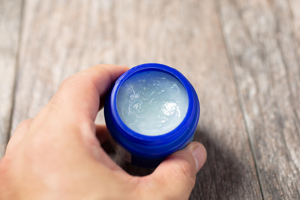 Someone holds a small jar of Vicks on top of a table