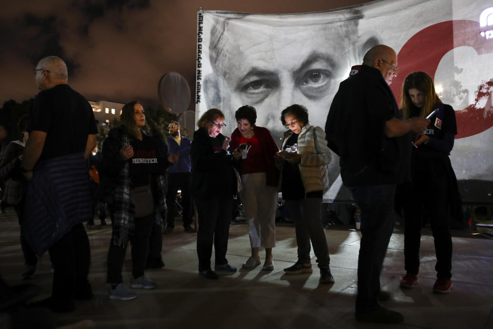 Protesters stand next to a banner showing Israeli Prime Minister Benjamin Netanyahu during rally calling for his resignation, in Tel Aviv, Israel, Saturday, Nov. 30, 2019. (AP Photo/Oded Balilty)