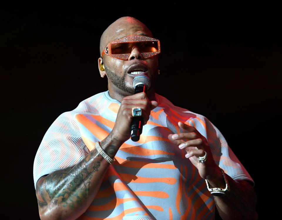 Flo rida signing in stage with a colorful outfit wearing sunglasses.