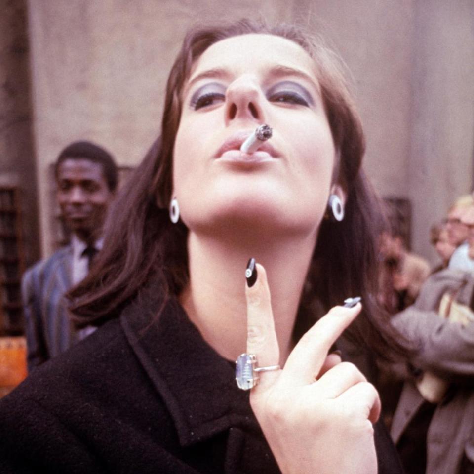 A woman smokes in the street, Soho, 1965.