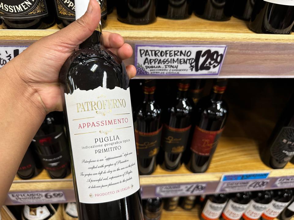 hand holding a bottle of trader joe's red wine in front of shelves of wine
