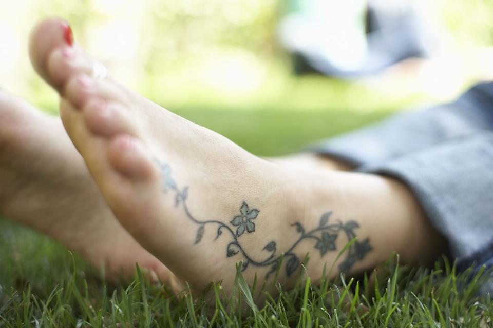 feet resting on grass with flower tattoo over ankle